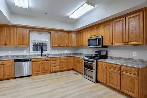 a kitchen with stainless steel appliances granite countertop wooden cabinets a stove top oven a sink and dishwasher with wooden floor