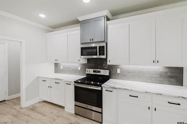 a large white kitchen with a sink dishwasher a stove and white cabinets with wooden floor