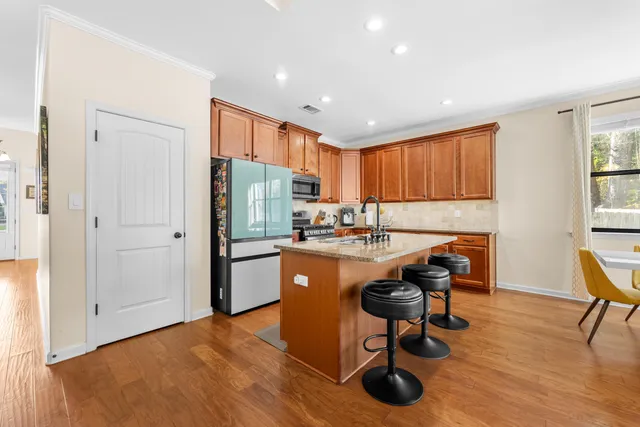 a kitchen with stainless steel appliances granite countertop a refrigerator a sink dishwasher a dining table and chairs with wooden floor