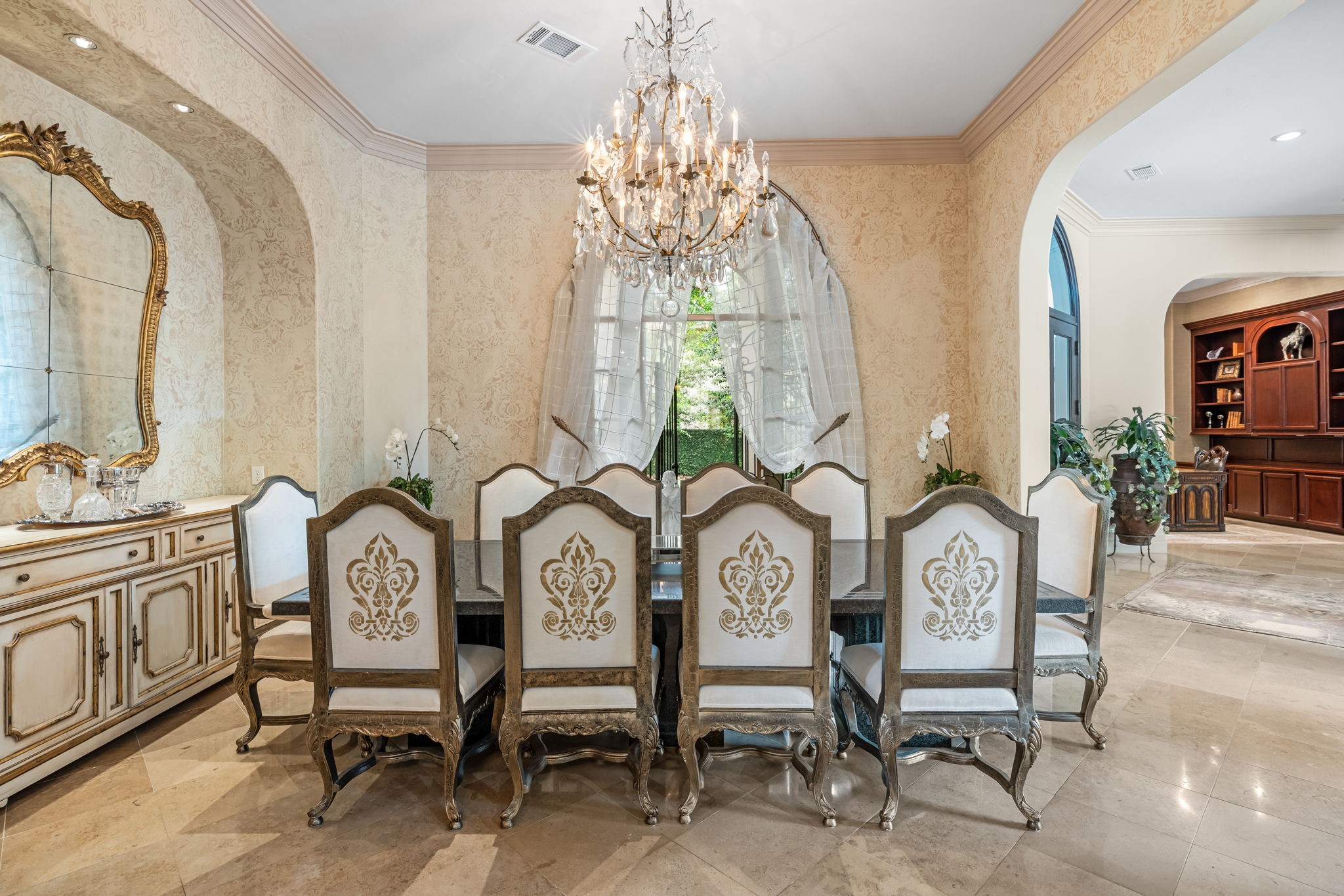 6 Mott Lane Houston, TX 77024 - Photo 25 of 50 Formal dining room exuding timeless elegance, featuring a statement chandelier, intricate wall finishes, and a beautifully coordinated dining set. Arched window with soft drapery fill the space with natural light.