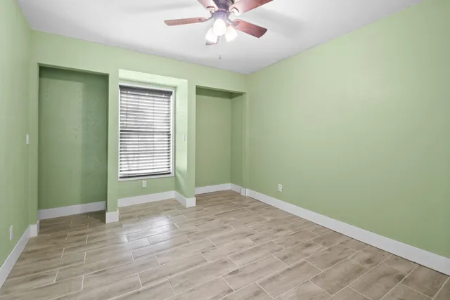 an empty room with wooden floor fan and windows