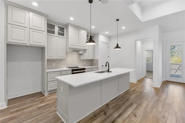 a large kitchen with stainless steel appliances granite countertop a sink dishwasher a refrigerator and white cabinets with wooden floor