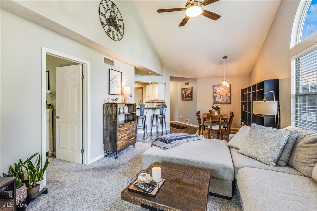 Carpeted living area featuring baseboards, visible vents, a ceiling fan, and high vaulted ceiling