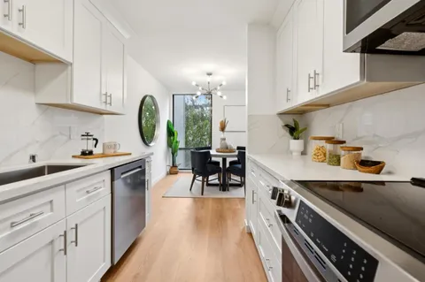 a kitchen with kitchen island a stove a sink dishwasher and white cabinets with wooden floor