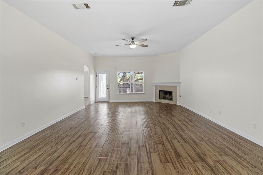 1011 St Helena Drive Leander, TX 78641 - Photo 3 of 11 Unfurnished living room featuring dark wood-style floors, a tile fireplace, a ceiling fan, and arched walkways