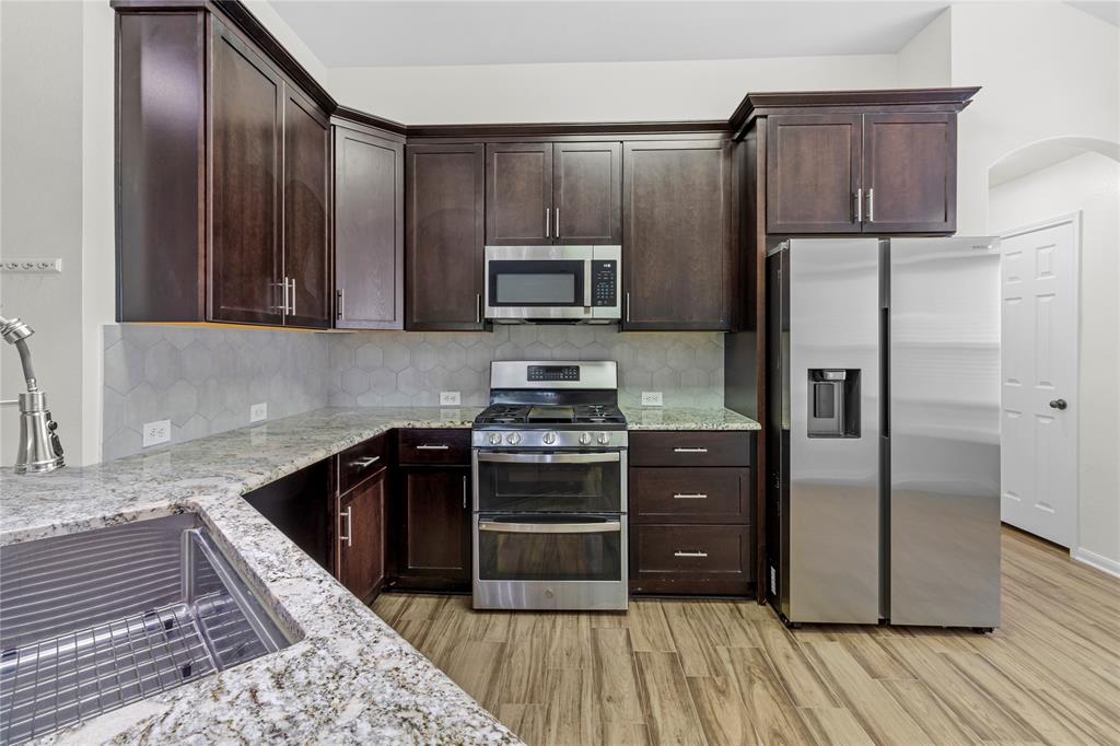 1011 St Helena Drive Leander, TX 78641 - Photo 4 of 11 Kitchen featuring appliances with stainless steel finishes, light stone counters, tasteful backsplash, and dark brown cabinets