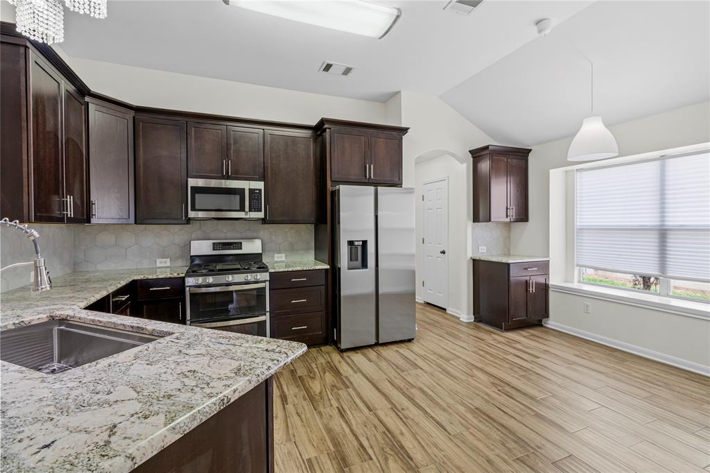 1011 St Helena Drive Leander, TX 78641 - Photo 5 of 11 Kitchen featuring tasteful backsplash, dark brown cabinets, appliances with stainless steel finishes, arched walkways, and light stone counters