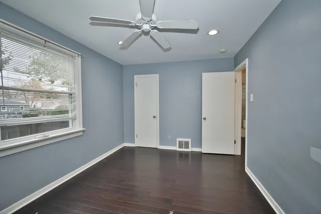 an empty room with wooden floor fan and windows