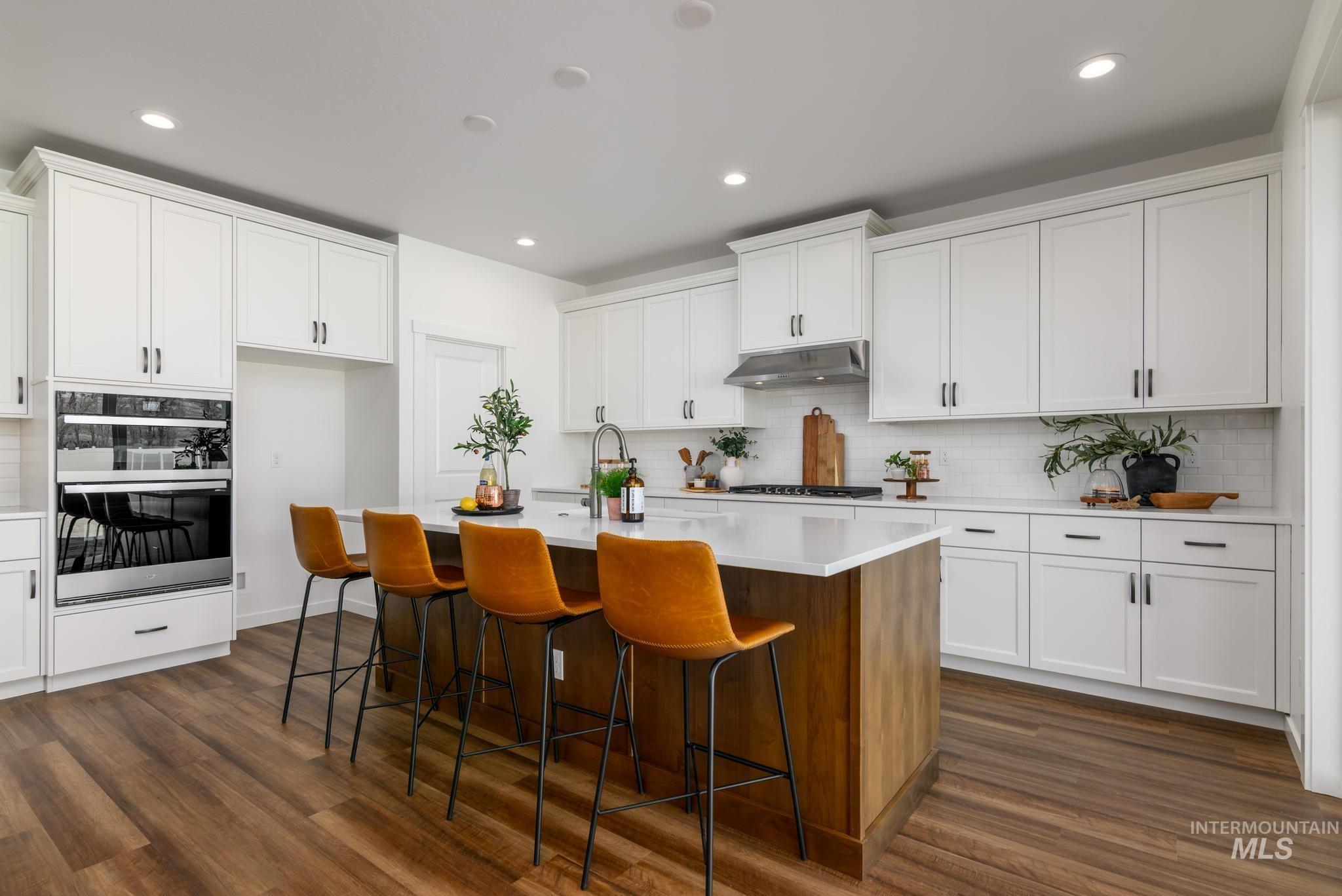 1244 Grassland Street Middleton, ID 83644 - Photo 6 of 10 Two tone kitchen featuring an island with sink, dual tone cabinets, a breakfast bar, dark wood-type flooring, and tasteful backsplash
