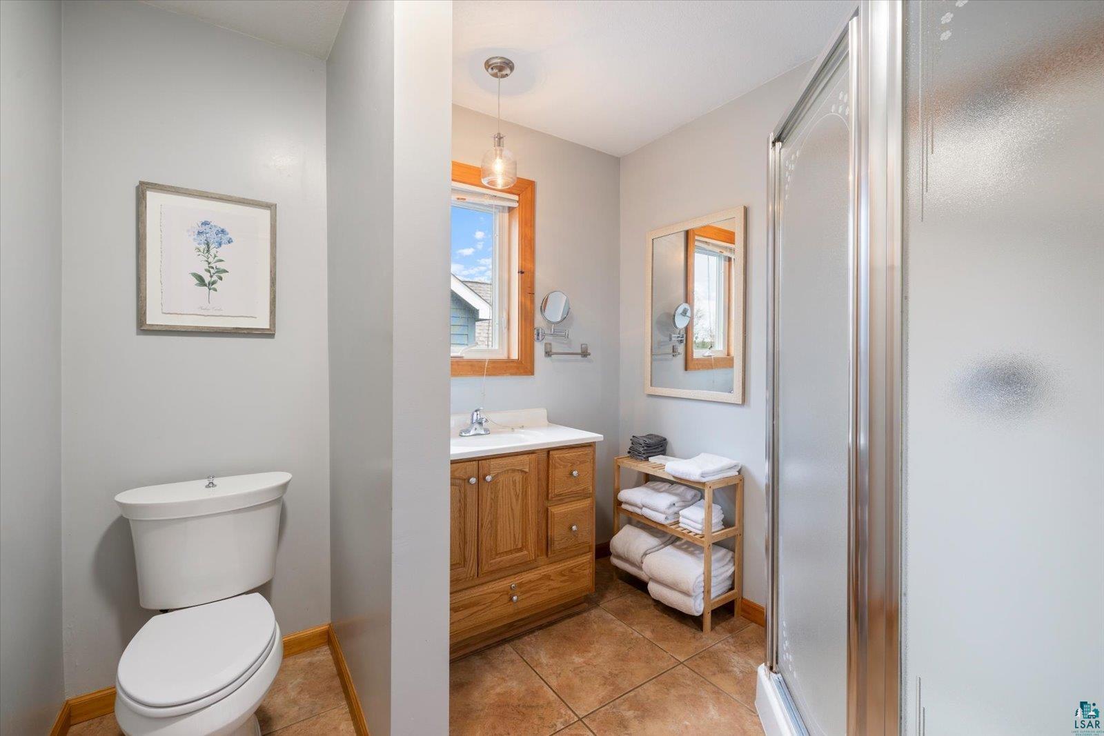 6266 Giants Ridge Road Biwabik, MN 55705 - Photo 21 of 37 Bathroom featuring a tile floor, wood-finish vanity with an integrated sink, a large mirror, a window with wood trim, and a frosted glass shower enclosure