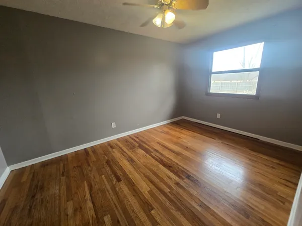 a view of an empty room with wooden floor and a window
