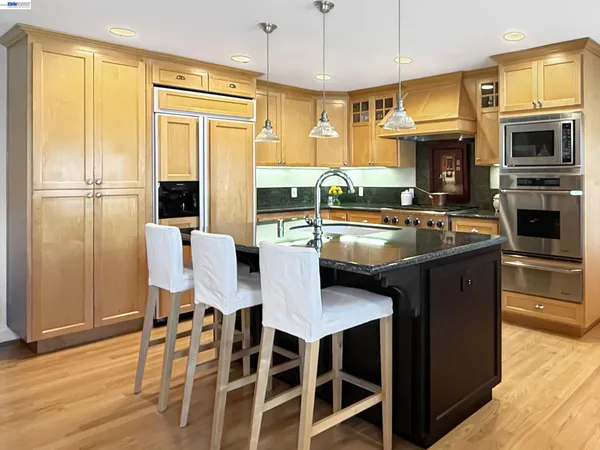 a kitchen with stainless steel appliances granite countertop a stove top oven a refrigerator a dining table and chairs with wooden floor