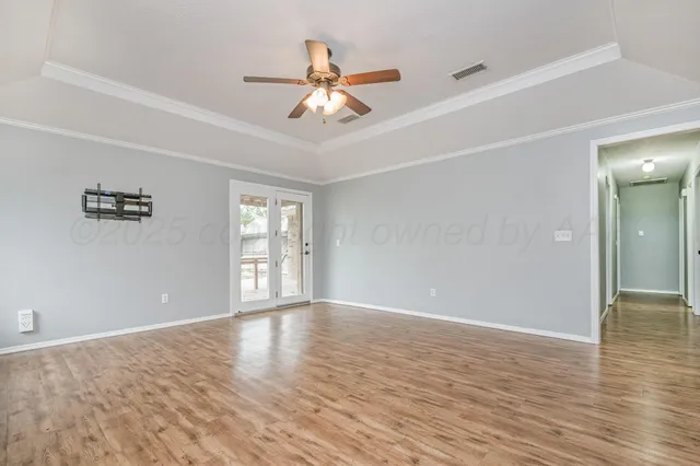 a view of an empty room with wooden floor and a ceiling fan