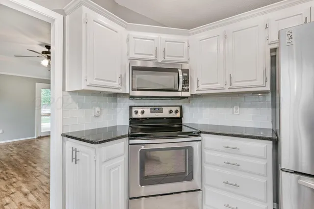 a kitchen with granite countertop white cabinets and stainless steel appliances