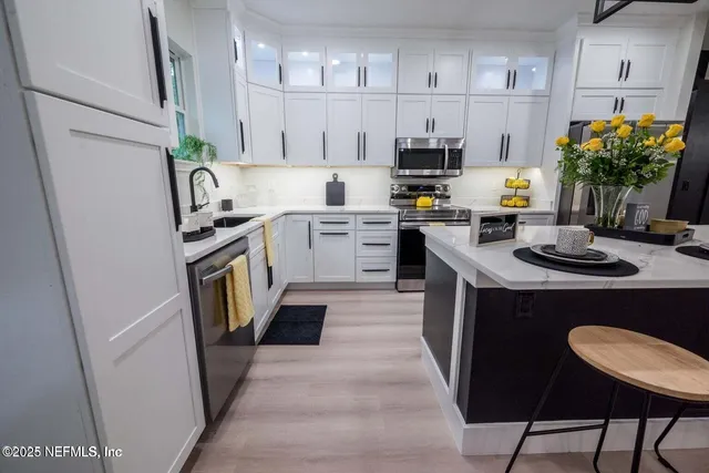 a kitchen with stainless steel appliances granite countertop a refrigerator a stove a sink dishwasher and white cabinets with wooden floor