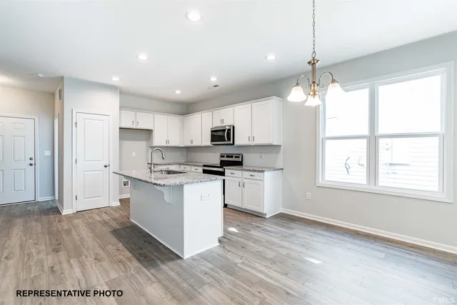 a kitchen with stainless steel appliances granite countertop a stove top oven a sink dishwasher a refrigerator and a dining table with wooden floor