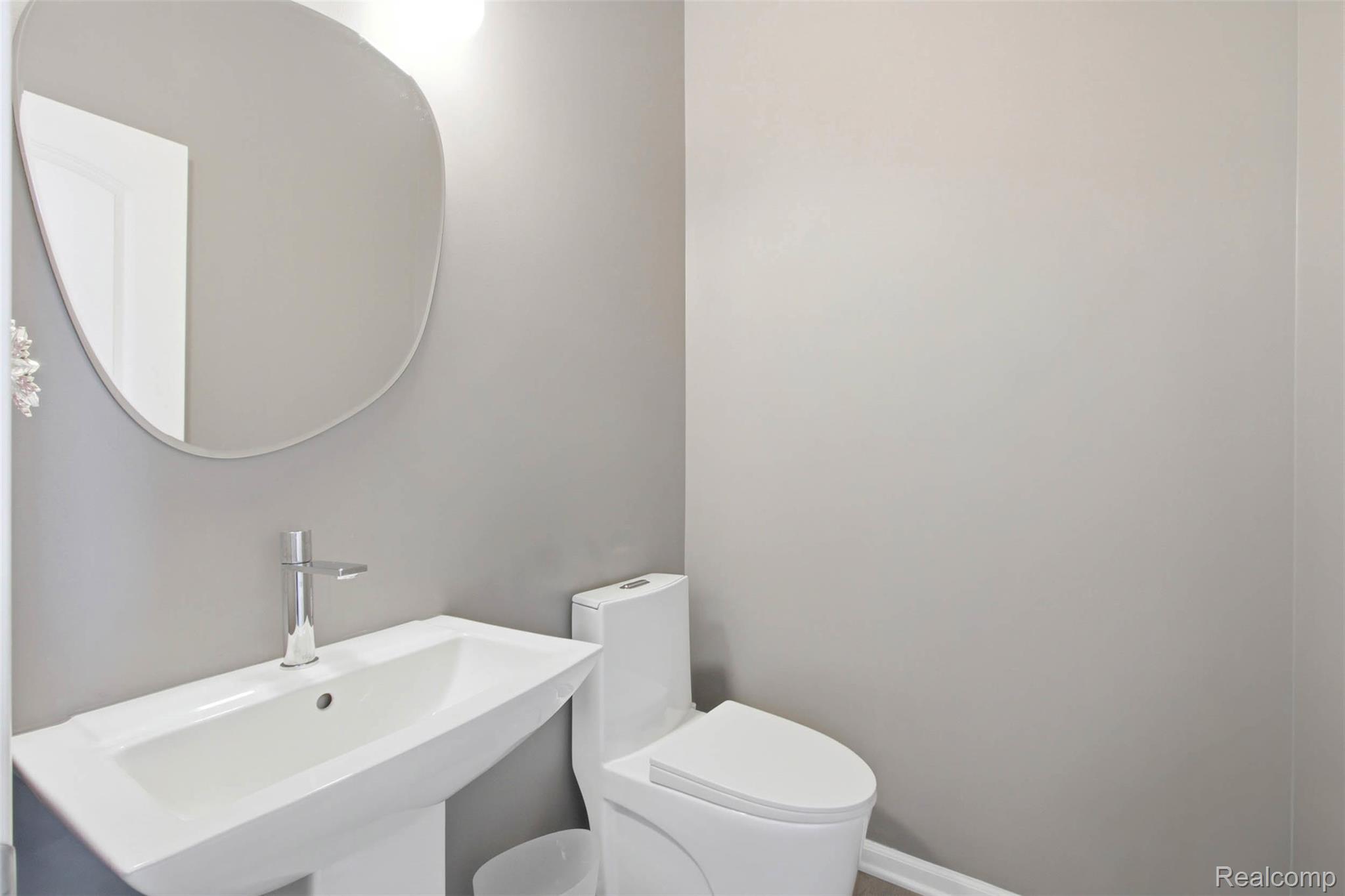 5085 Ridge Lane Warren, MI 48092 - Photo 5 of 29 Pedestal sink with a polished chrome faucet, an organic-shaped mirror, and a contemporary toilet