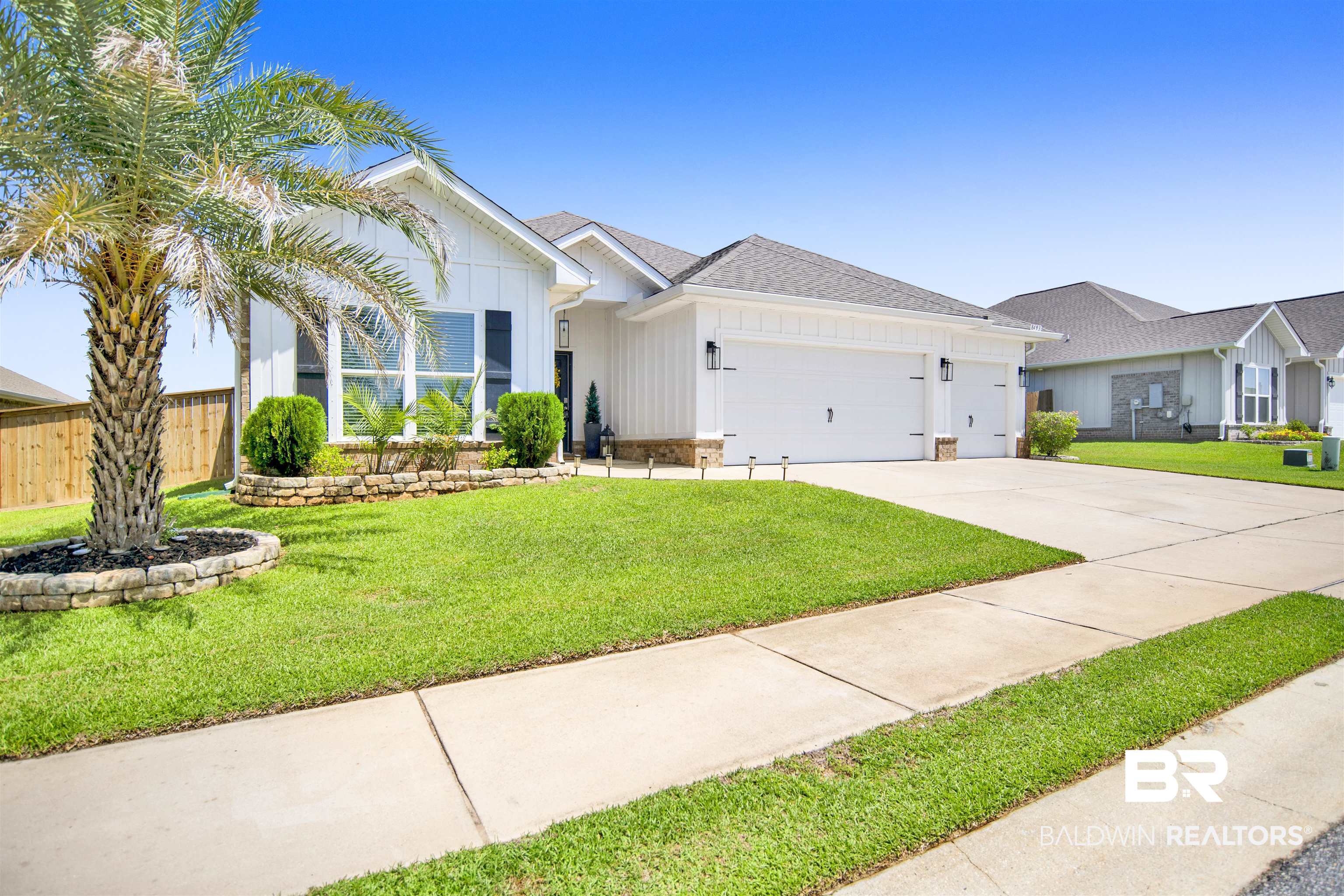8493 Bronze Lane Foley, AL 36535 - Photo 1 of 38 White contemporary exterior featuring board and batten siding, a two-car garage with black carriage-style hardware, and a stone-trimmed landscape bed