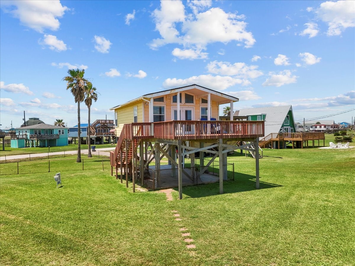 819 Seashell Drive Surfside Beach, TX 77541 - Photo 10 of 36 This photo shows a charming elevated beach house with a large wooden deck, surrounded by a spacious, grassy yard. The home offers picturesque views, perfect for enjoying coastal living.