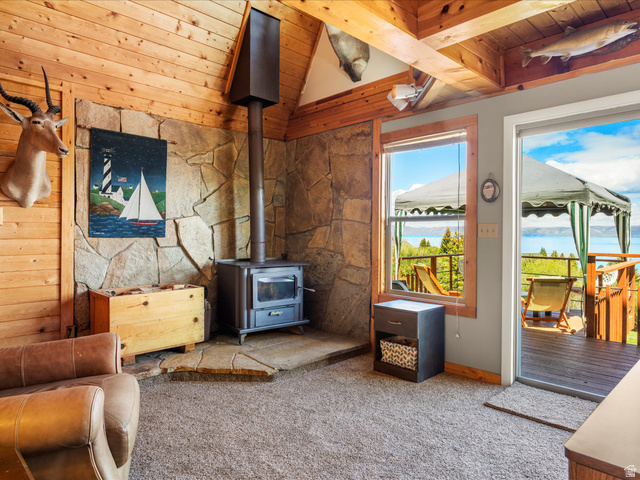 371 Lewis Loop, Unit 29 Fish Haven, ID 83287 - Photo 18 of 40 Living area featuring a stone accent wall, a freestanding wood-burning stove, wood plank wall paneling, and an exposed wood beam ceiling