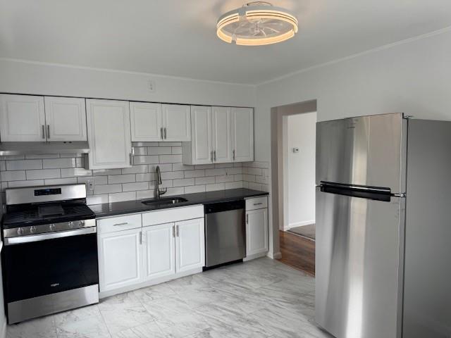 Kitchen featuring white cabinetry, under cabinet range hood, a sink, dark countertops, and appliances with stainless steel finishes