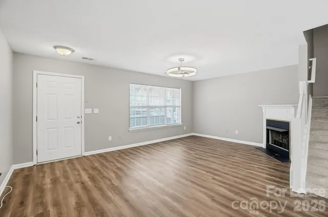 a view of an empty room with wooden floor fireplace and a window