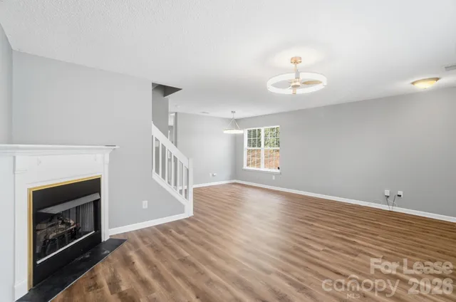 a view of an empty room with wooden floor fireplace and a window