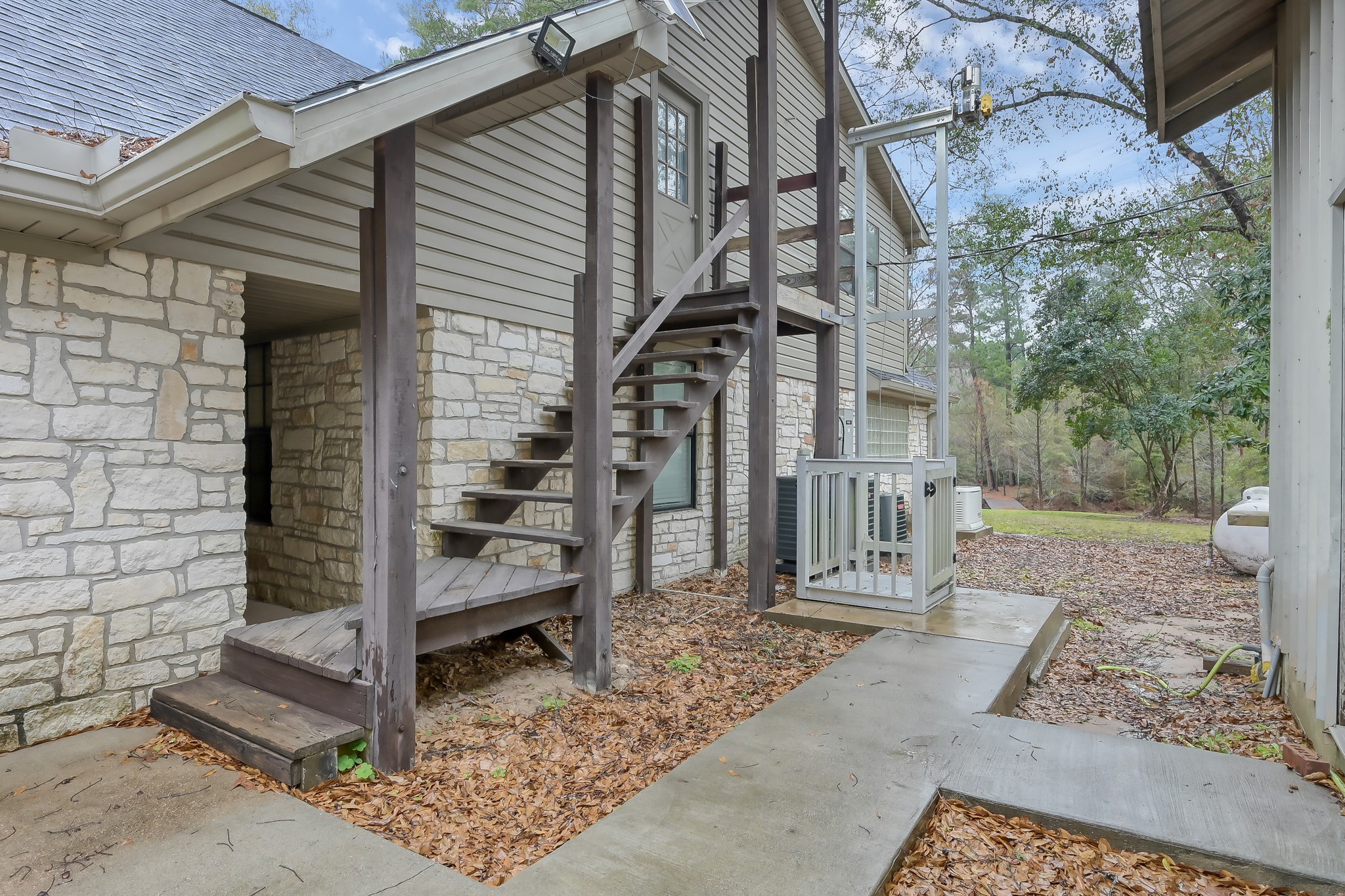 80 Nettie Phillips Road Coldspring, TX 77331 - Photo 44 of 49 Staircase to Guest Bedroom as well as an exterior elevator. Concrete pathways lead to the porte-cochere to the left and the barn to the right.