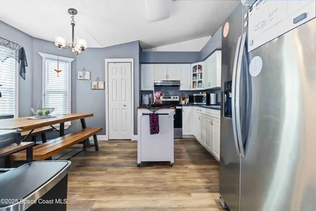 a kitchen with stainless steel appliances granite countertop a refrigerator a sink dishwasher a stove and a dining table with wooden floor