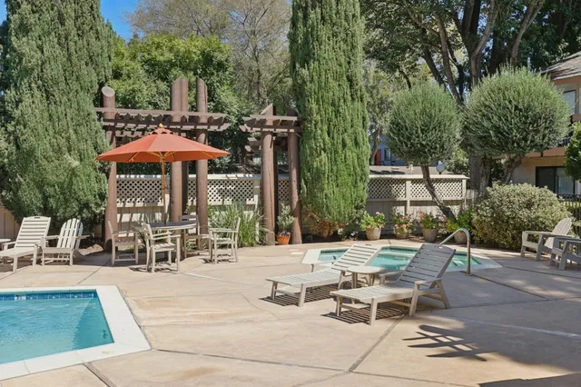a view of a patio with a dining table and chairs under an umbrella with large trees
