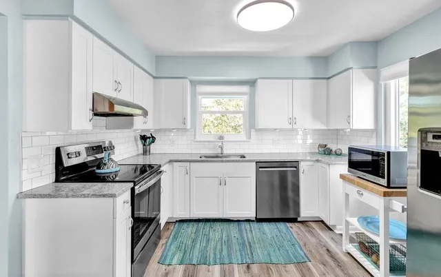 a kitchen with granite countertop a sink cabinets stainless steel appliances and a window