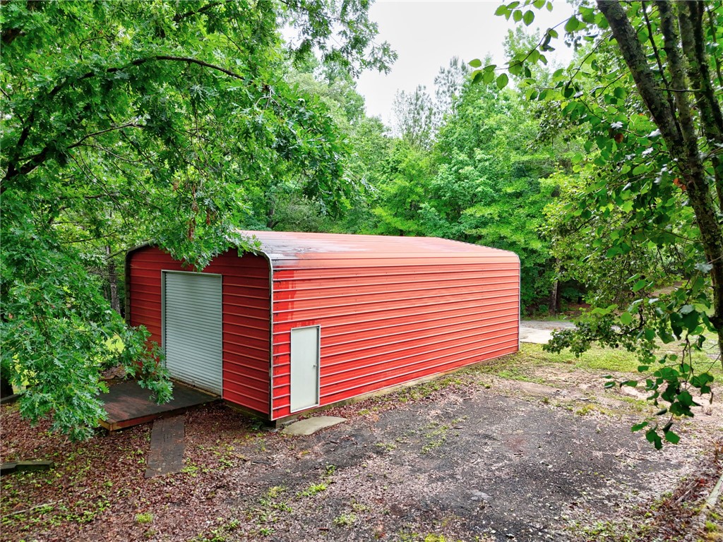 237 Spring Valley Road Liberty, SC 29657 - Photo 33 of 50 A vibrant red metal structure with roll-up doors, offering versatile storage amidst verdant trees.