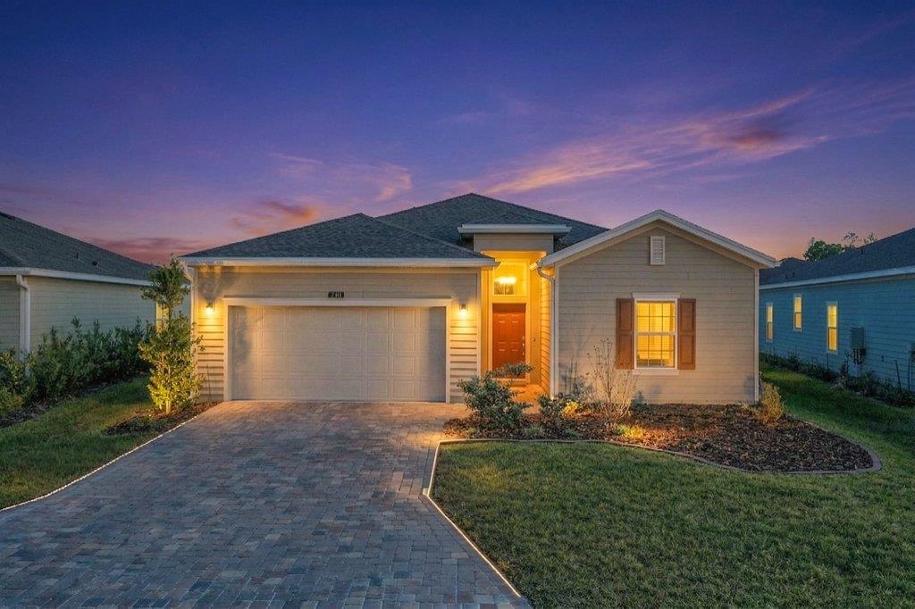Ranch-style home featuring an attached garage, decorative driveway, and a lawn