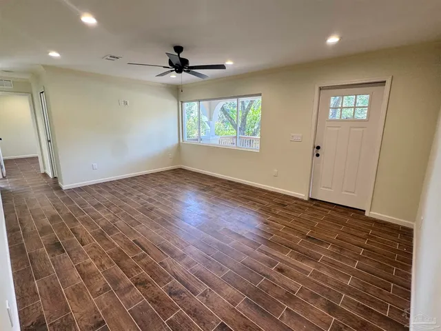 an empty room with wooden floor fan and windows