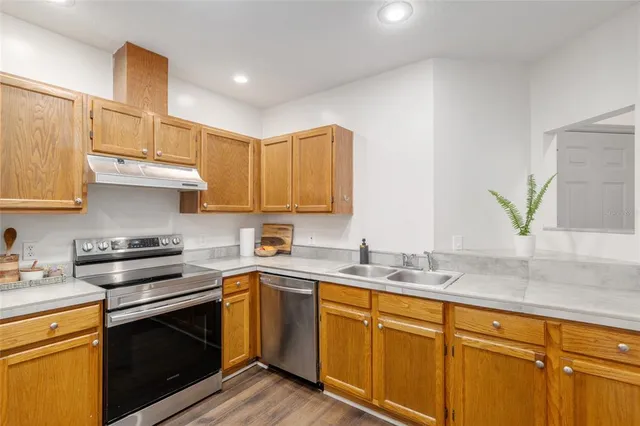 a kitchen with stainless steel appliances granite countertop a refrigerator a stove and a sink with wooden floor