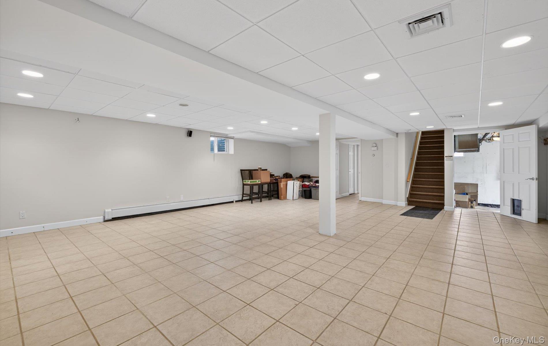 16 East Slope Road Bayville, NY 11709 - Photo 34 of 48 Finished lower level with neutral tiled flooring, recessed lighting, drop ceiling, and a visible staircase with wood treads