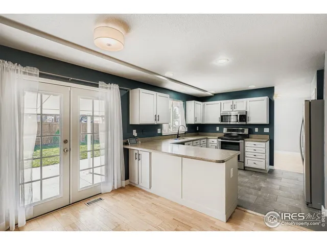 a kitchen with stainless steel appliances kitchen island granite countertop a refrigerator oven a sink dishwasher and white cabinets with wooden floor