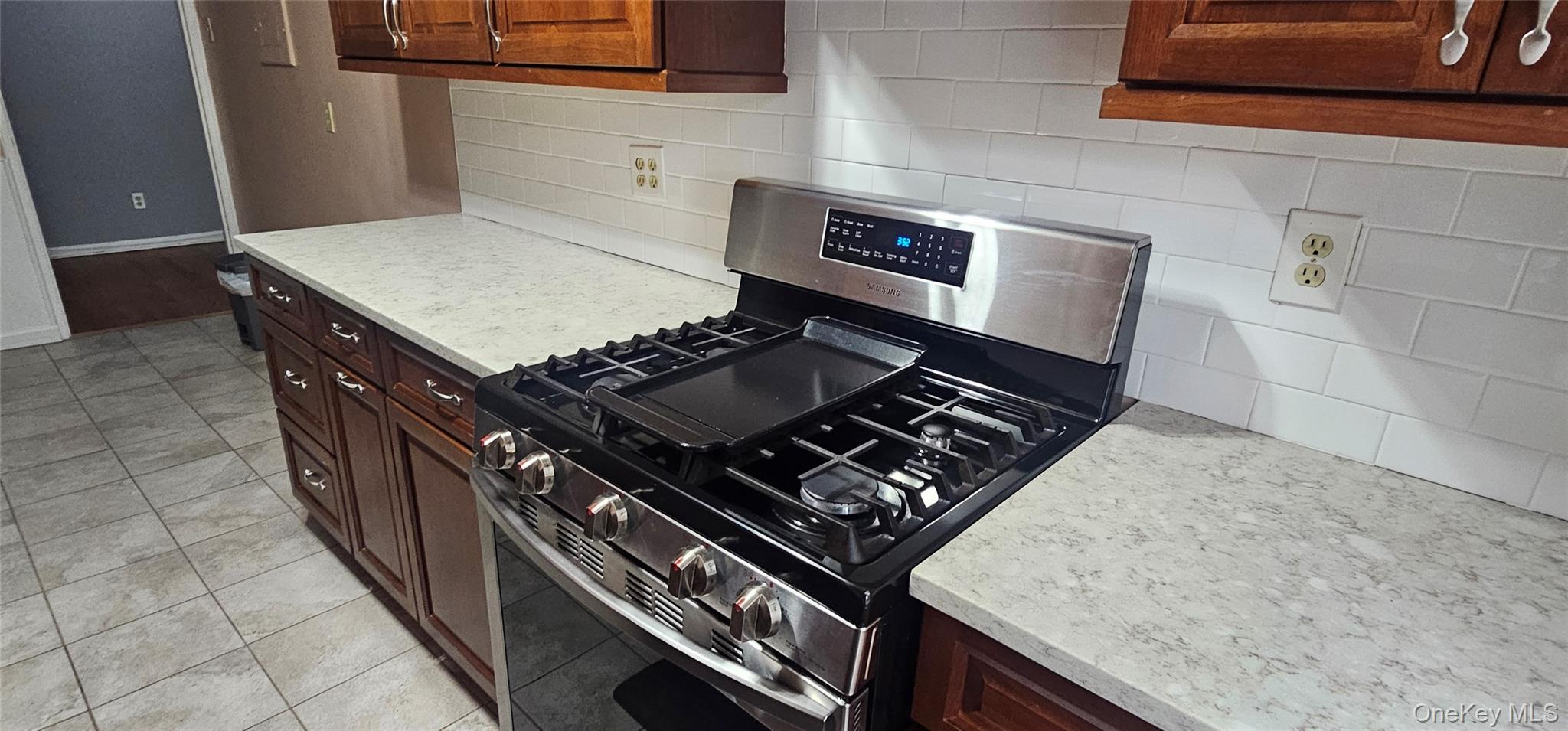 126 Church Street, Unit 2D New Rochelle, NY 10805 - Photo 6 of 15 Kitchen with stainless steel gas range oven, decorative backsplash, light tile patterned floors, dark brown cabinetry, and light stone countertops