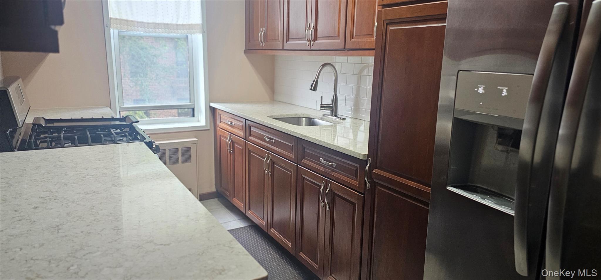 126 Church Street, Unit 2D New Rochelle, NY 10805 - Photo 8 of 15 Kitchen featuring stainless steel appliances, light stone countertops, backsplash, radiator heating unit, and dark tile patterned floors