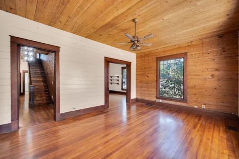 an empty room with wooden floor chandelier and windows