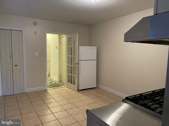 a view of a refrigerator in kitchen and an empty room in wooden floor