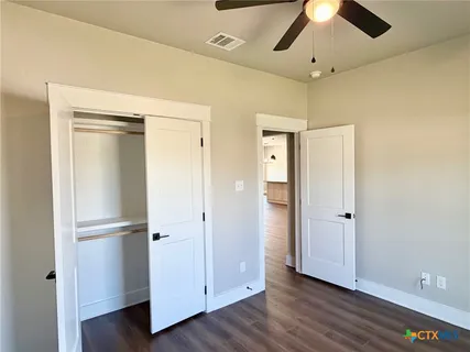 a view of an empty room with wooden floor and a ceiling fan