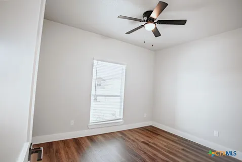 an empty room with wooden floor ceiling fan and window