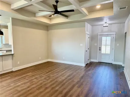 a view of an empty room with wooden floor and a ceiling fan