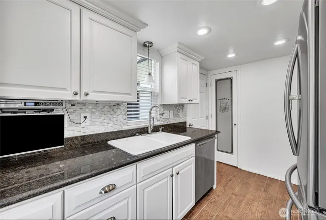 a kitchen with granite countertop a sink stainless steel appliances and white cabinets