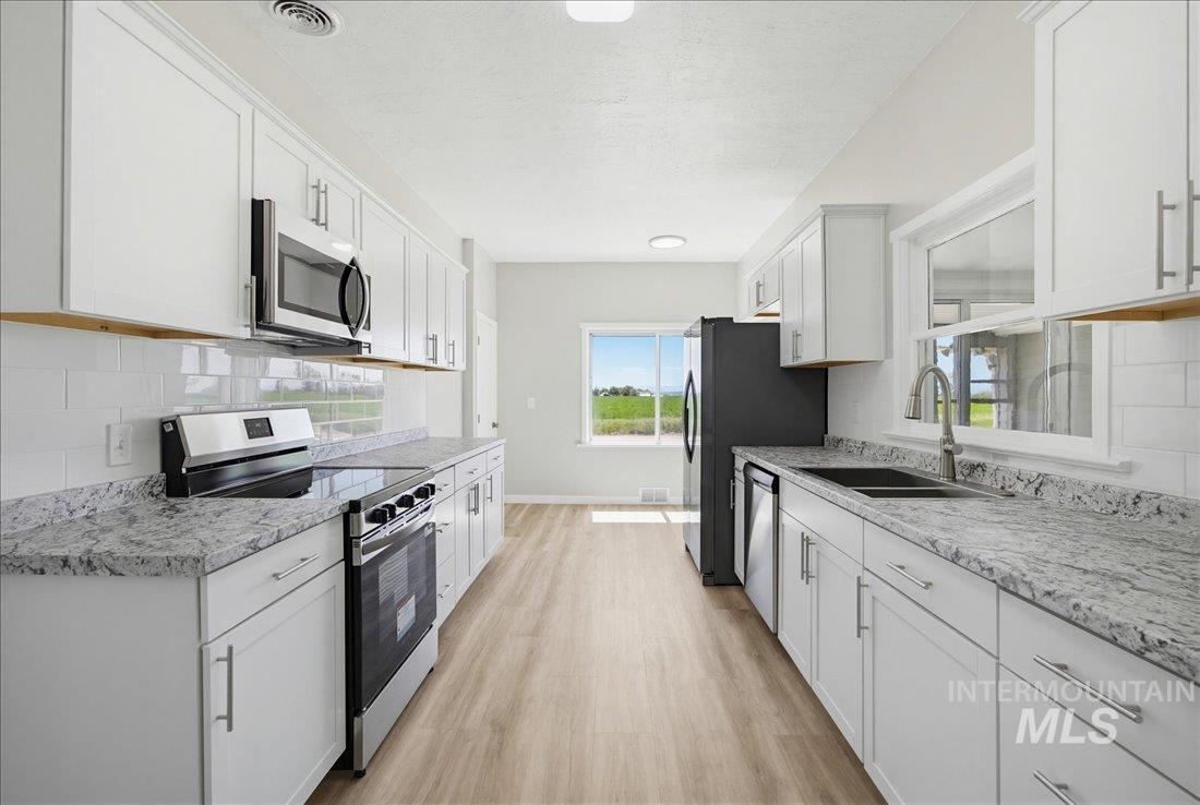 30013 Apple Valley Road Parma, ID 83660 - Photo 5 of 25 Modern kitchen featuring white shaker cabinetry, stainless steel appliances, speckled countertops, a subway tile backsplash, and light wood-finish flooring
