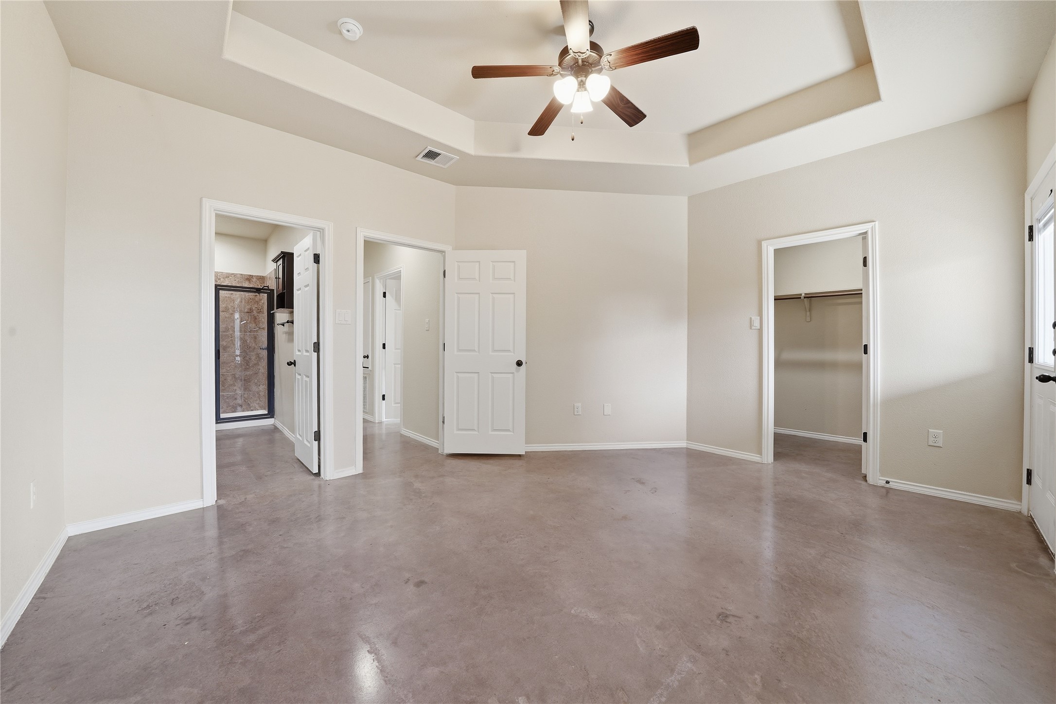 533 Jack Rabbit Lane, Unit A Buda, TX 78610 - Photo 22 of 34 A spacious primary bedroom features a tray ceiling with a fan and durable polished concrete flooring.