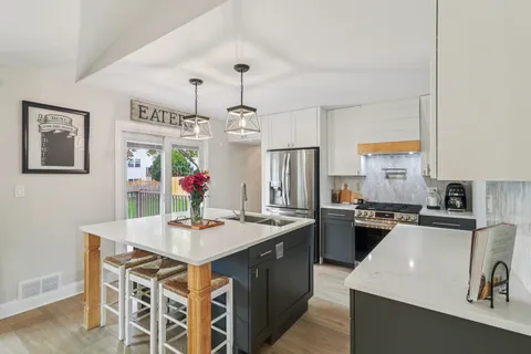 a kitchen with a stove a sink a kitchen island with chairs and wooden floor