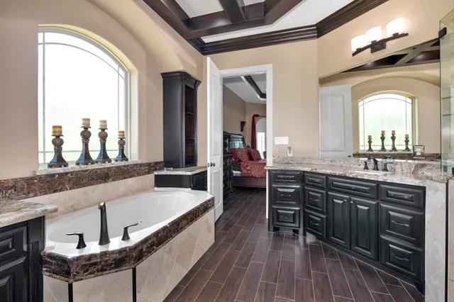 a bathroom with a granite countertop sink a mirror and a bathtub next to a window