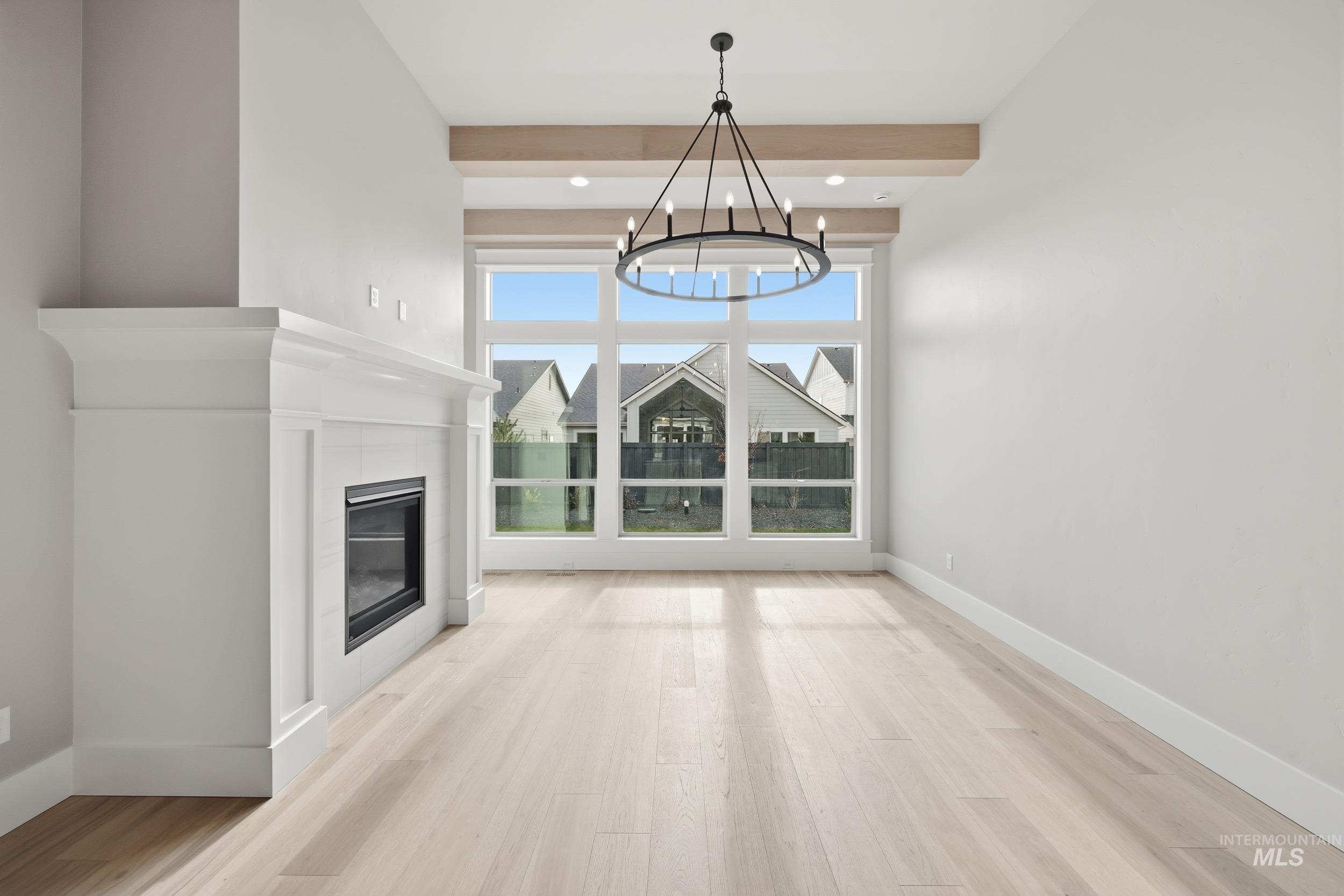 1035 East Crescendo Street Meridian, ID 83642 - Photo 2 of 50 Unfurnished living room with a tiled fireplace, light wood finished floors, beam ceiling, and a chandelier